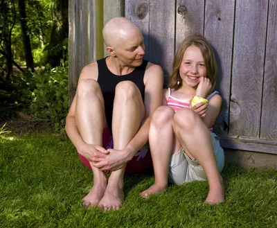 Woman sits with child in the grass in front of a fence